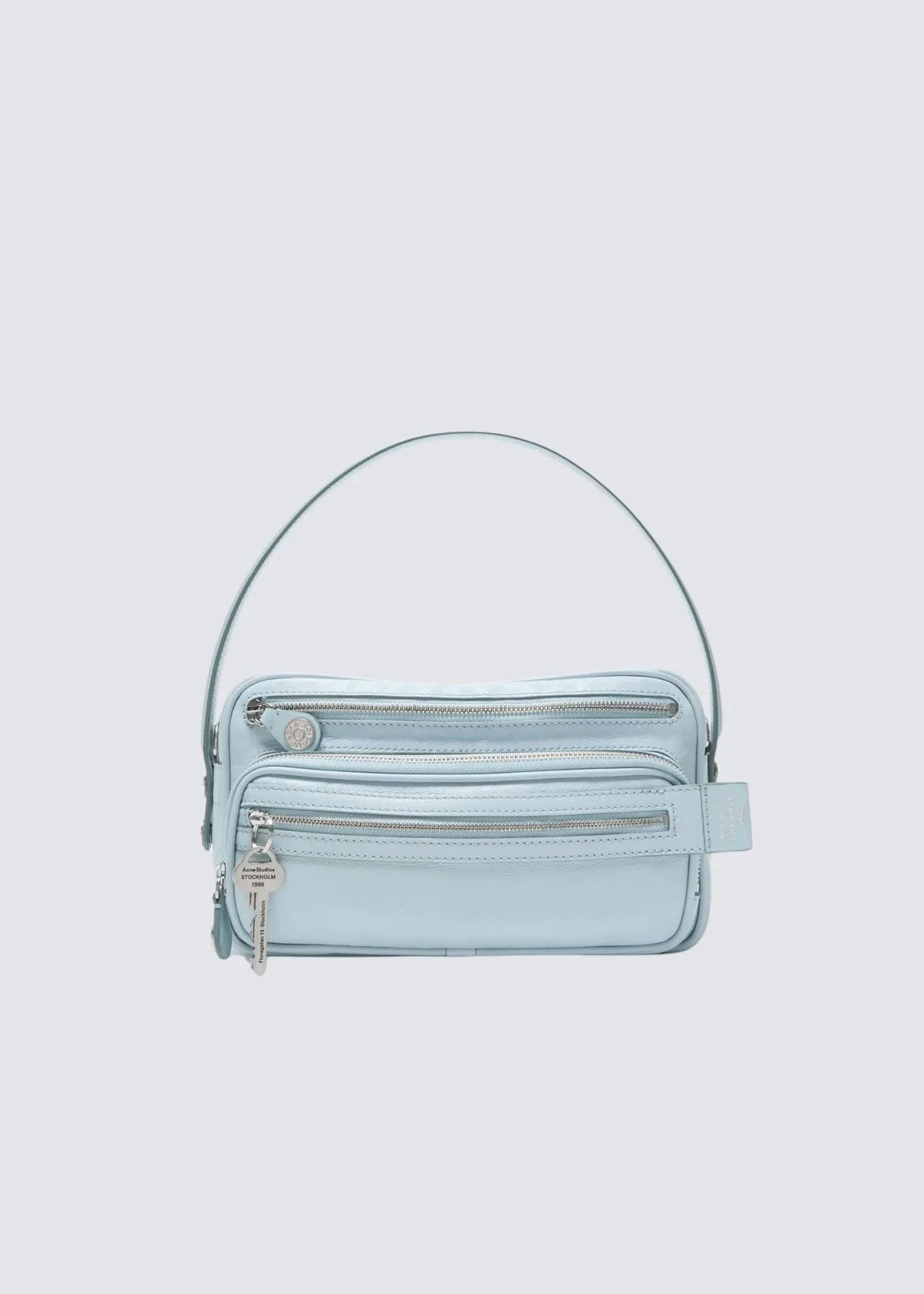 Acne Studios Camero Party Handtasche von vorne freistehend mit Riemen, Blick auf 2 Reißverschluss Fächer und Acne Studios Schlüsselanhänger.
