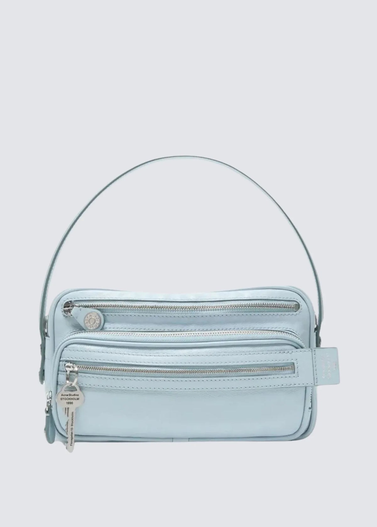 Acne Studios Camero Party Handtasche von vorne freistehend mit Riemen, Blick auf 2 Reißverschluss Fächer und Acne Studios Schlüsselanhänger.