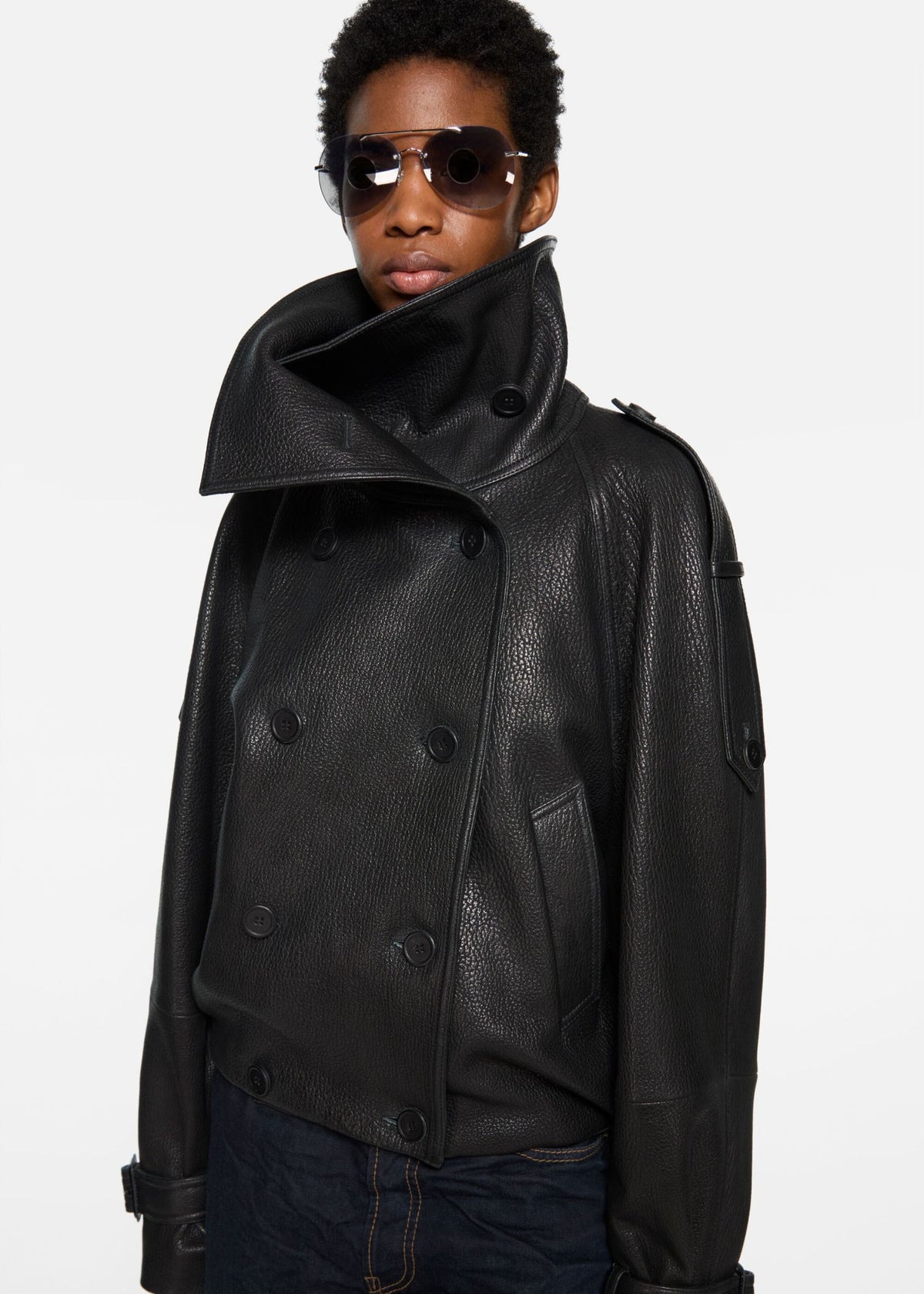Model trägt Acne Studios Lederjacke in schwarz, , Seitenansicht mit Fokus auf die Doppelreiher-Knopfleiste und Schulterriemen im Trenchcoat-Look, weißer Hintergrund