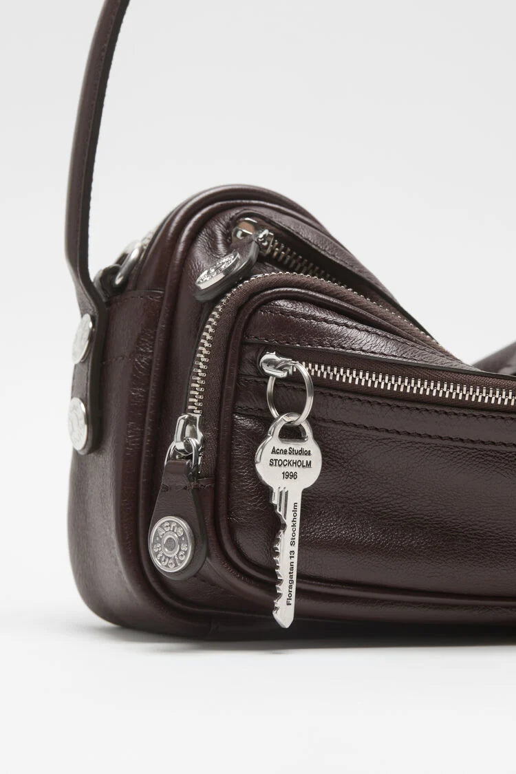 Glattleder Tasche in Braun mit kurzem Tragegriff, abnehmbarer Schulterriemen.
Großes Hauptfach mit Reißverschluss,
Reißverschluss-Fächer außen. Schlüsselanhänger sowie
Silberne Hardware. Detail Shot Hardware.