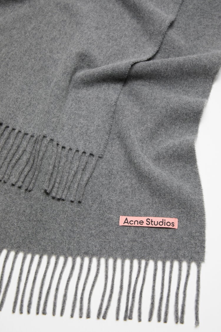 Graue Wollschal mit Pinken Logo Etikett. Ausgefranstes Ende. Detail Shot Logo.