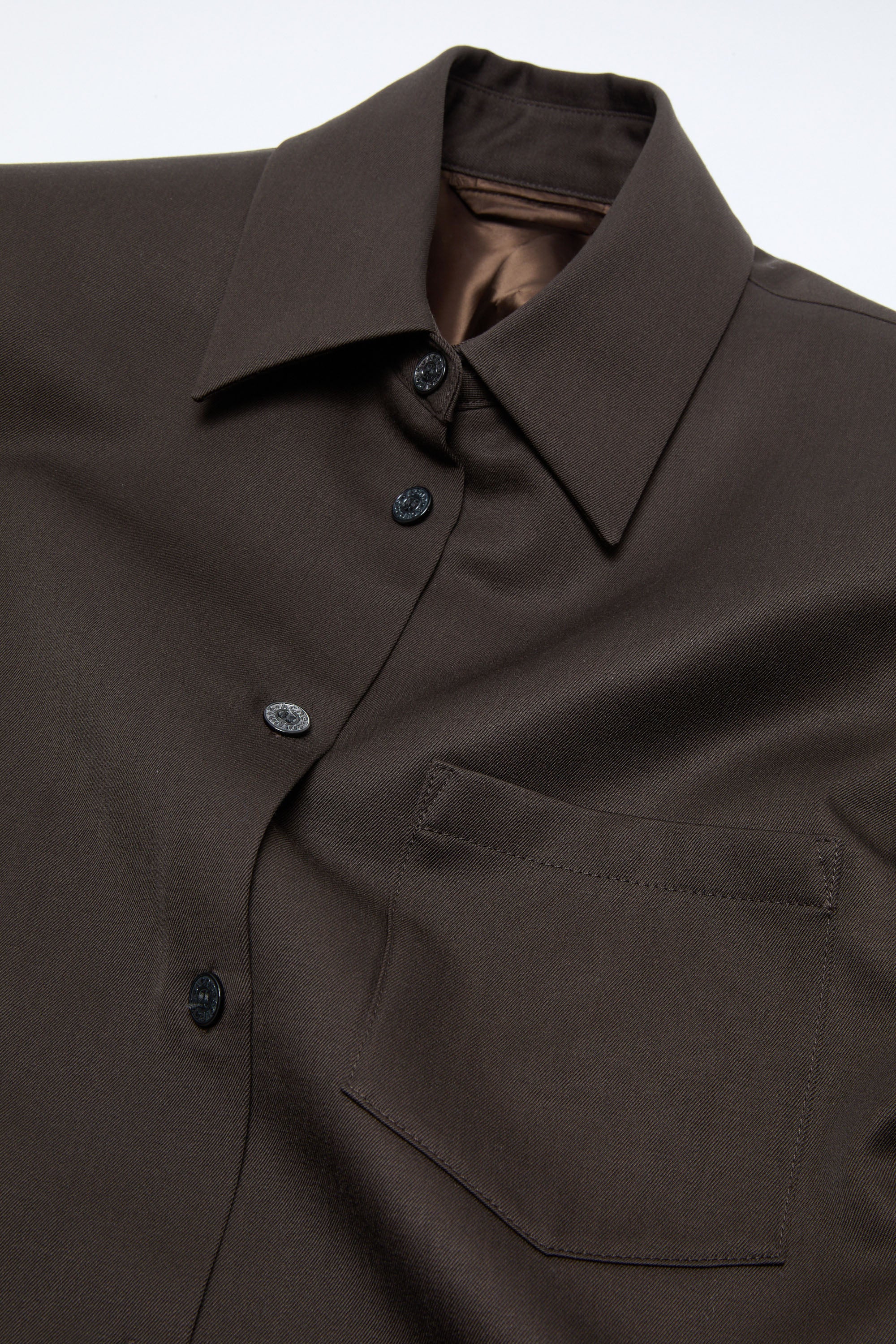 Acne Studios Hemdjacke in schokobraun aus Schurwolle, Detailansicht des Kragens und der Knopfleiste. Auf der rechten Seite befindet sich eine aufgesetzte Brusttasche