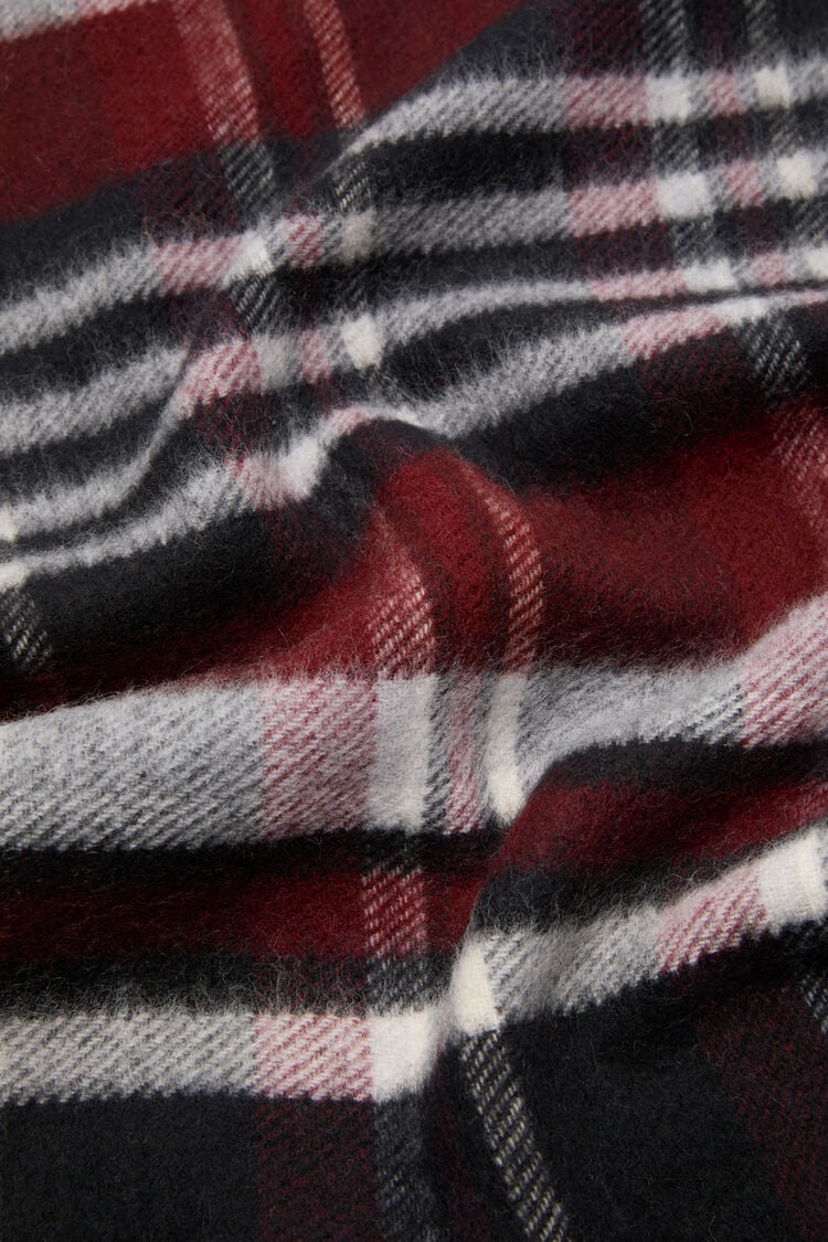 Karierter Wollschal in Schwarz/Bordeaux mit Logoprägung am Ende. Detail Shot Musterung. 