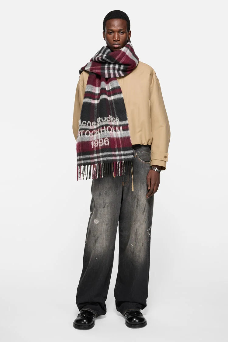 Karierter Wollschal in Schwarz/Bordeaux mit Logoprägung am Ende. Model Bild.