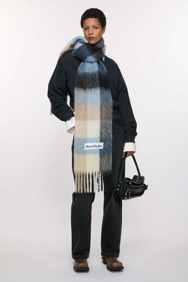 Schal aus Mohair Mischung, Kariert in einer hellen Farbmischung als Creme/Taupe Farben sowie Blau Tönen. Logo Etikett in Weiß. Model Foto. 