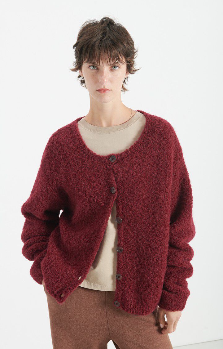 Cardigan am Model in der Halbnahen. Der rechte Arm ist angewinkelt, der Cardigan ist nur an den oberen beiden Knöpfen zugeknöpft. 