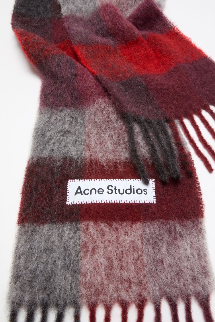 Acne Studios Woll-Mohair-Schal mit einem rot-schwarzen Karo-Muster und Fransen am Ende - Nahaufnahme vom Acne-Logo