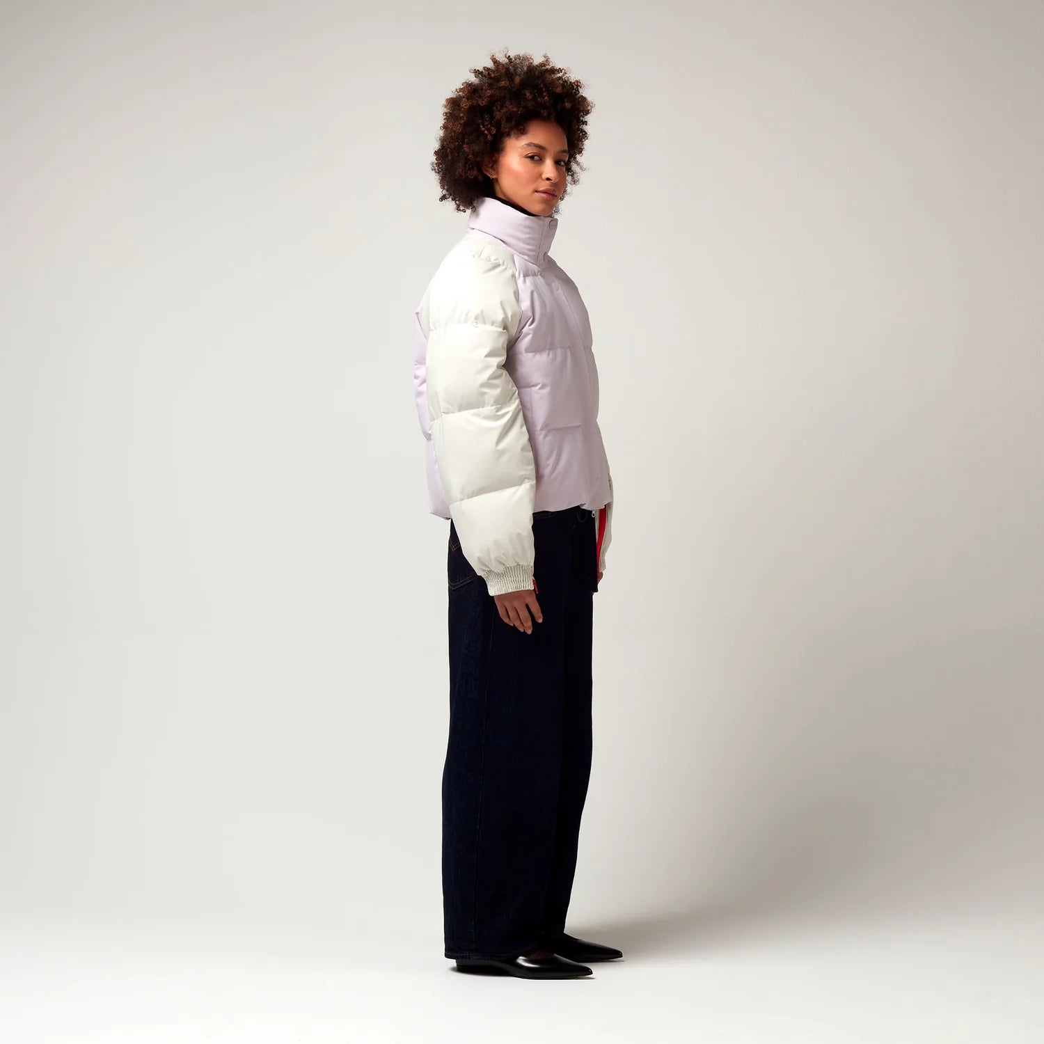 Kurz geschnittene Jacke in Creme, Rosa mit Roten Details. Die Jacke verfügt über einen Stehkragen, einen Reißverschluss mit magnetischer Knopfleiste sowie Reißverschlüssen an den Ärmel, hochreichend bis zur Armbeuge. Model Bild, seitliche Ansicht.