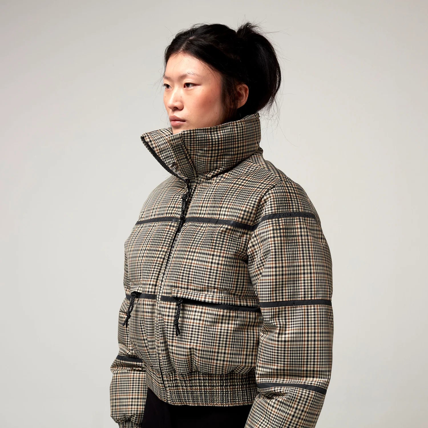 Bomberjacke mit Stehkragen, Reißverschluss und Zwei Taschen. Saum an Ärmeln sowie Bauch mit Gummizug. Karo Muster in Beige Braun. Model Bild, Detail Aufnahme.