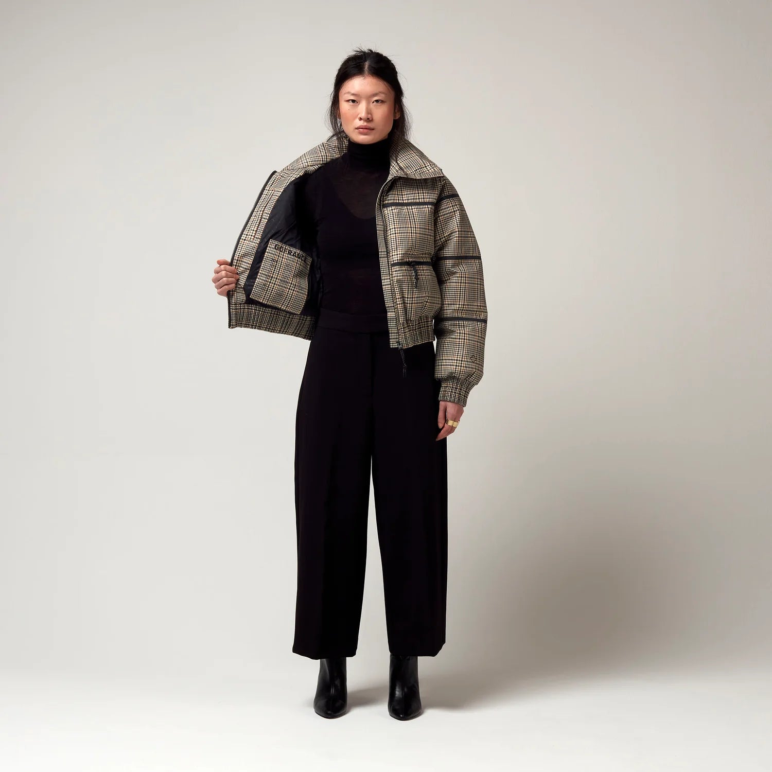 Bomberjacke mit Stehkragen, Reißverschluss und Zwei Taschen. Saum an Ärmeln sowie Bauch mit Gummizug. Karo Muster in Beige Braun. Leicht geöffnete Jacke, Innenfutter erkennbar Model Bild. 