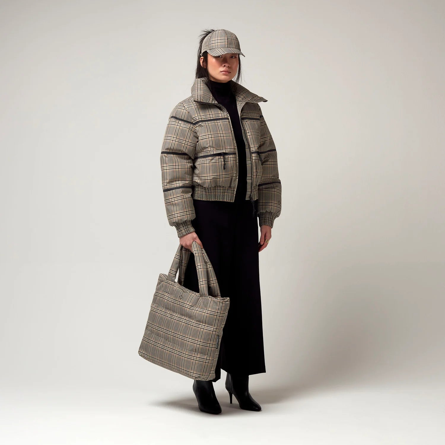 Bomberjacke mit Stehkragen, Reißverschluss und Zwei Taschen. Saum an Ärmeln sowie Bauch mit Gummizug. Karo Muster in Beige Braun. Mit passender Kappe sowie Tragetasche. Model Bild.