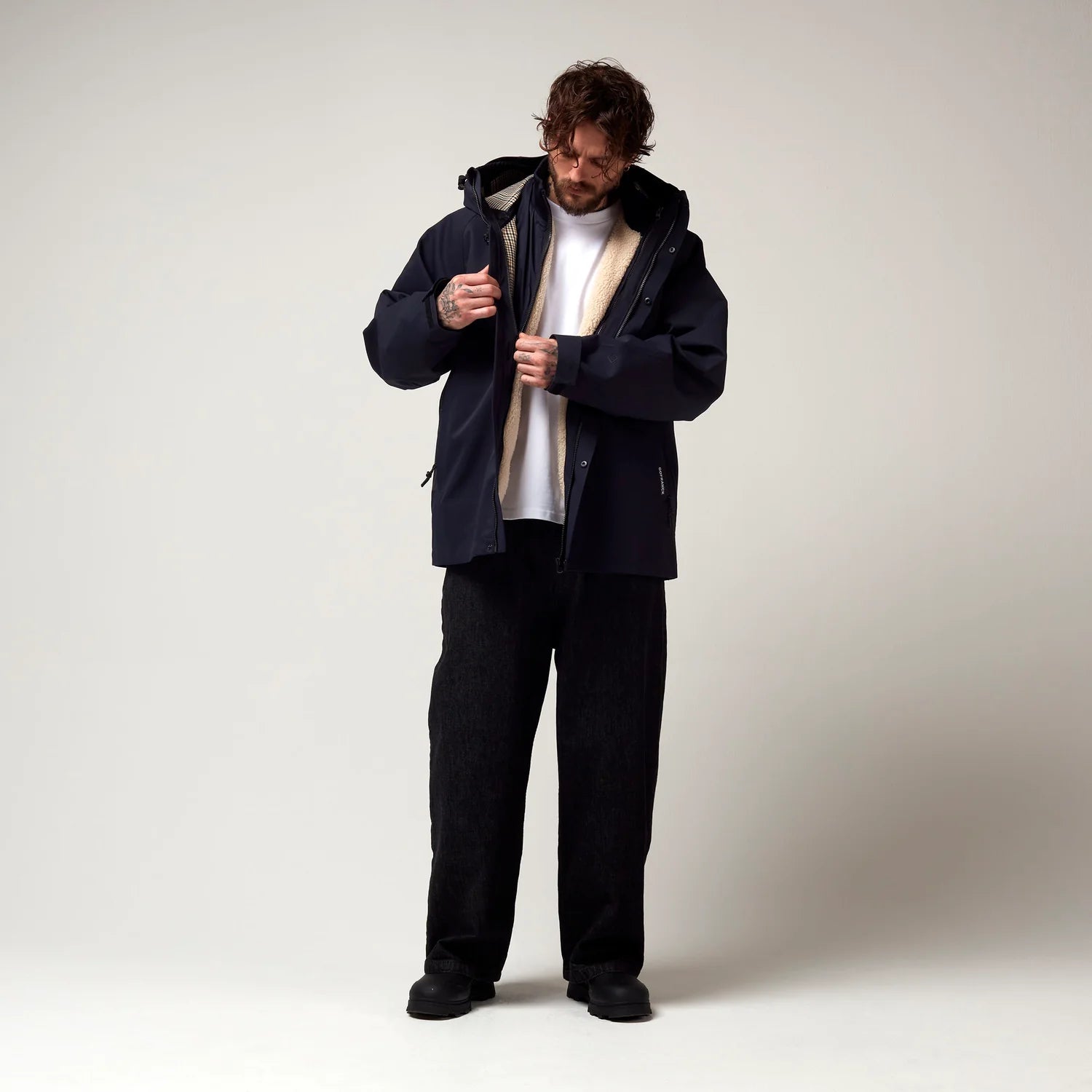 Dunkel Blaue  kurz geschnittene Jacke, mit Verstellbarer Kapuze sowie verstellbarem Saum an den Händen. Schwarze Hardware. Jacke leicht geöffnet, Innenjacke erkennbar. Model Bild. 