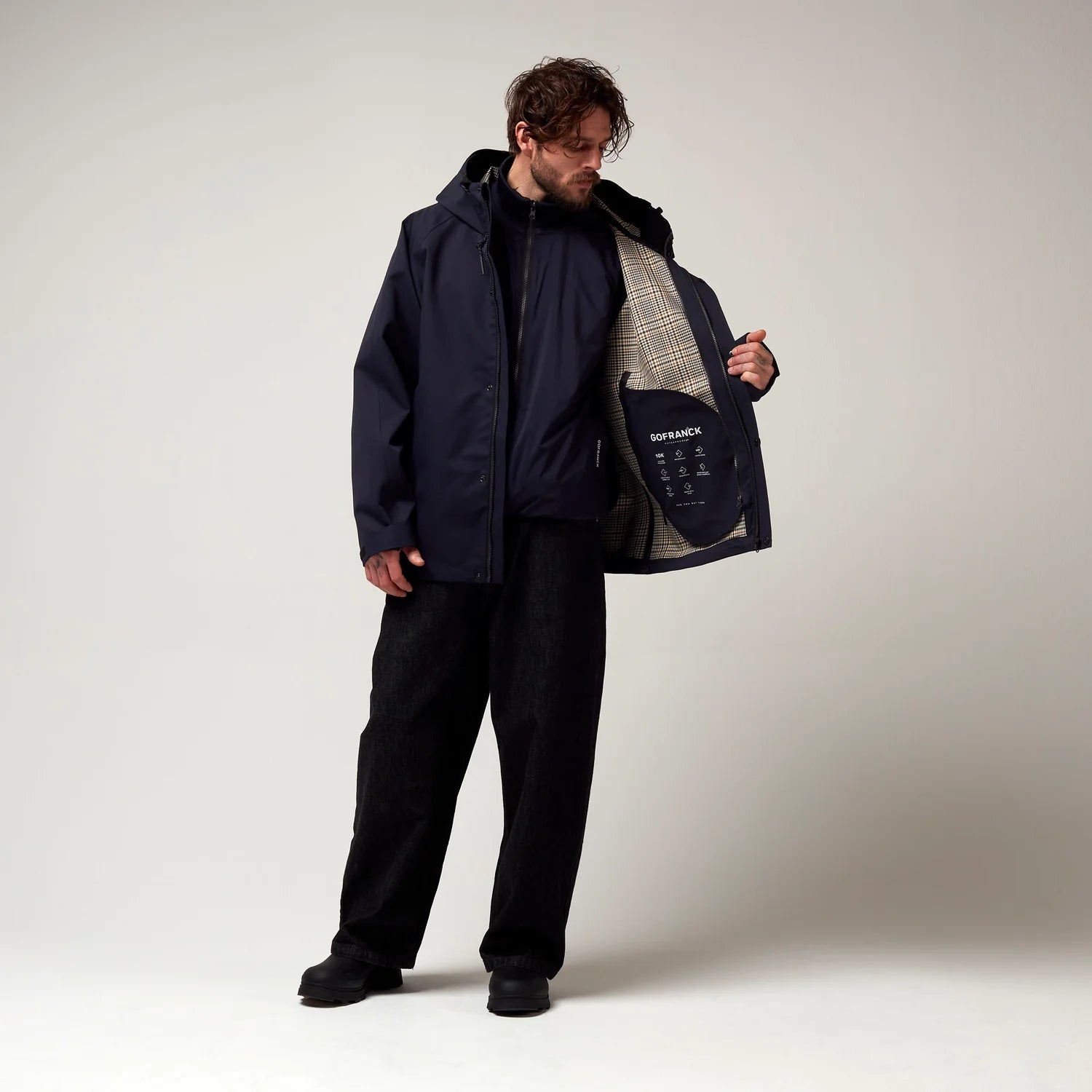 Dunkel Blaue  kurz geschnittene Jacke, mit Verstellbarer Kapuze sowie verstellbarem Saum an den Händen. Schwarze Hardware. Jacke leicht geöffnet, Innenjacke geschlossen. Model Bild. 