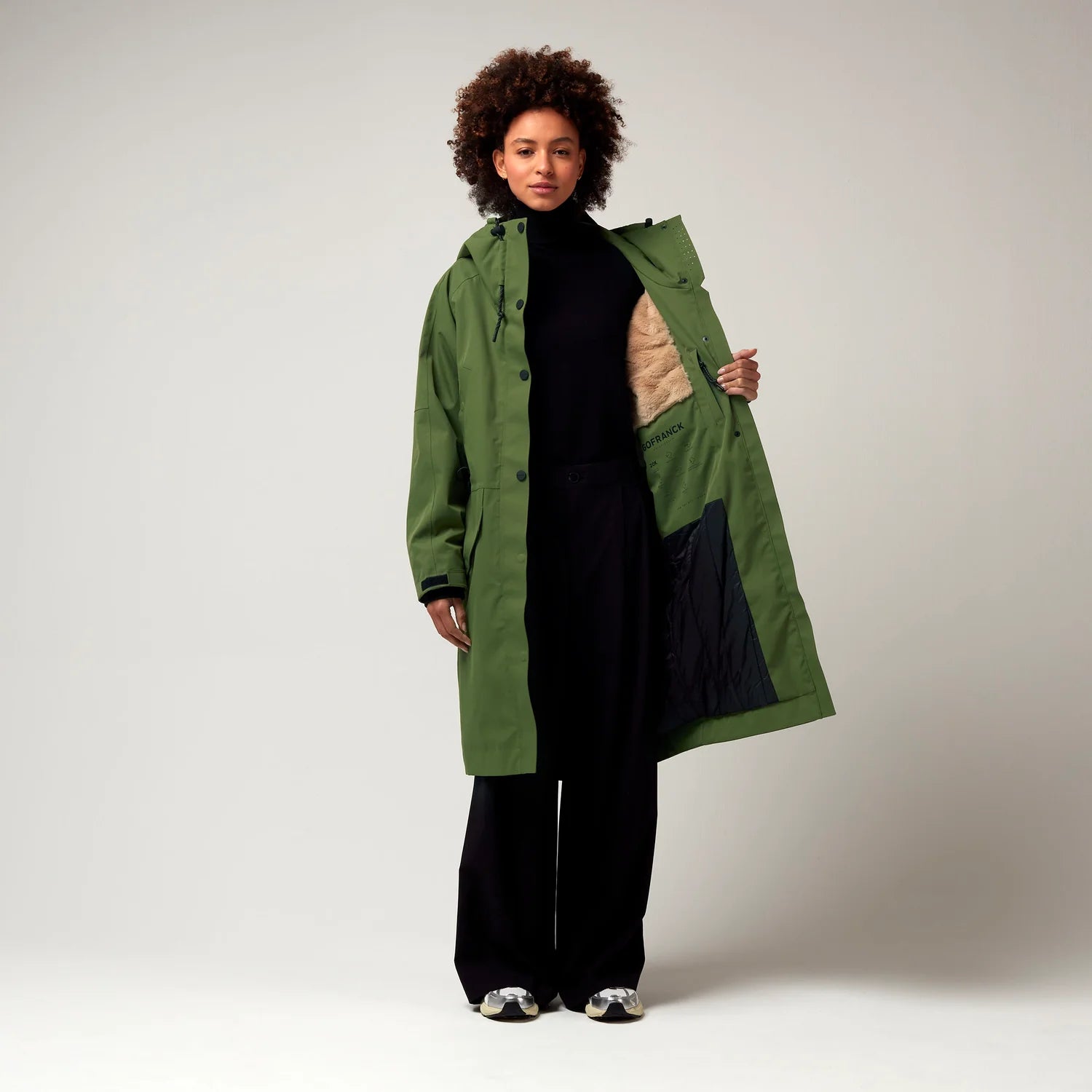 Grüner Parker, mit verstellbarer Kapuze, Seitentaschen sowie Saum mit Daumen Loch. Glatte Oberfläche. Schwarze Hardware. Model Foto Ganzkörper Aufnahme, leicht geöffnete Jacke, Innenfutter erkennbar.