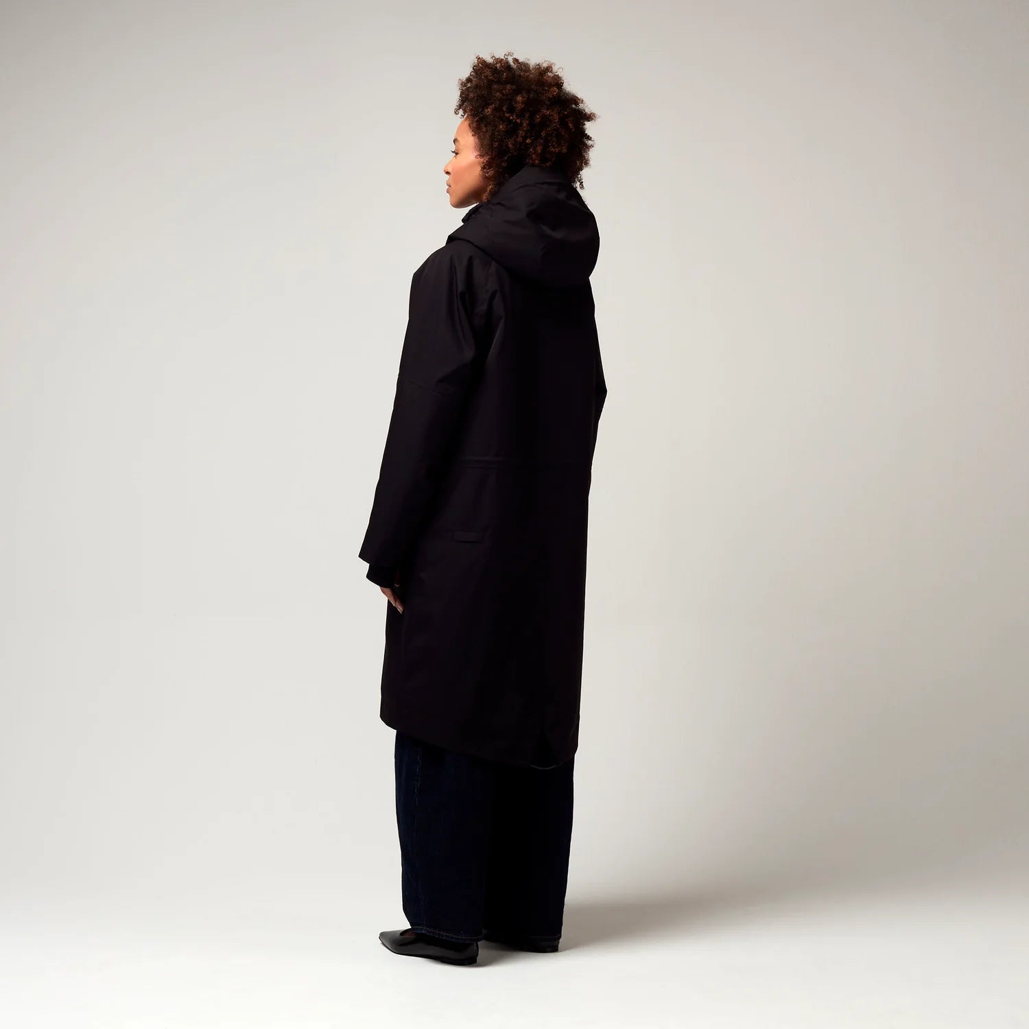 Schwarzer Parker, mit verstellbarer Kapuze, Seitentaschen sowie Saum mit Daumen Loch. Glatte Oberfläche. Model Foto Ganzkörper Aufnahme, seitliche Ansicht.