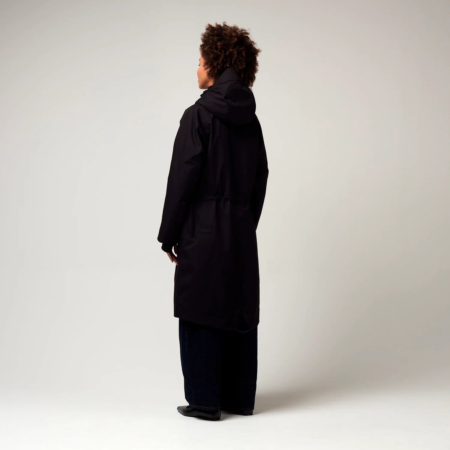 Schwarzer Parker, mit verstellbarer Kapuze, Seitentaschen sowie Saum mit Daumen Loch. Glatte Oberfläche. Model Foto Ganzkörper Aufnahme, seitliche Ansicht.