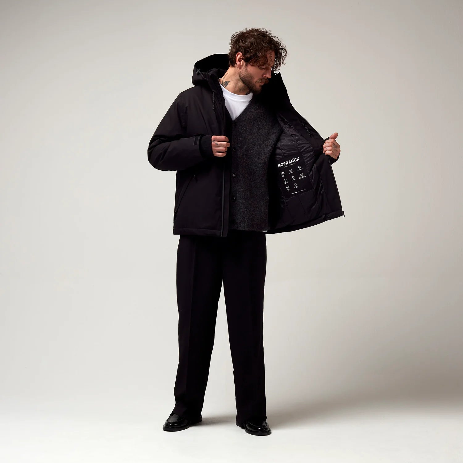 Kurz geschnittene Schwarze Jacke, mit verstellbarer Kapuze, seitlichen Jacke Taschen sowie schwarzer Hardware. Saum an den Ärmeln mit Daumen Loch. Leicht geöffnet Innenfutter erkennbar. Model Bild.