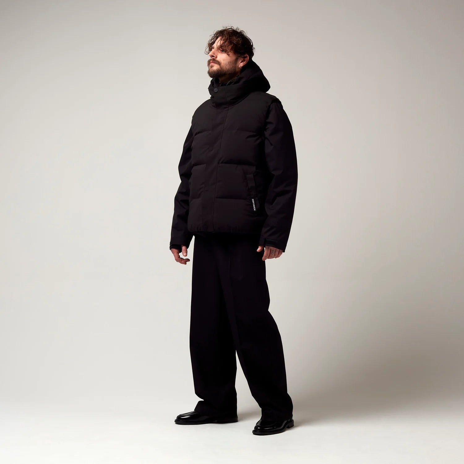 Kurz geschnittene Schwarze Jacke, mit verstellbarer Kapuze, seitlichen Jacke Taschen sowie schwarzer Hardware. Saum an den Ärmeln mit Daumen Loch. Dazugehörige schwarze Steppweste über der bereist beschrieben Jacke. Model Bild.