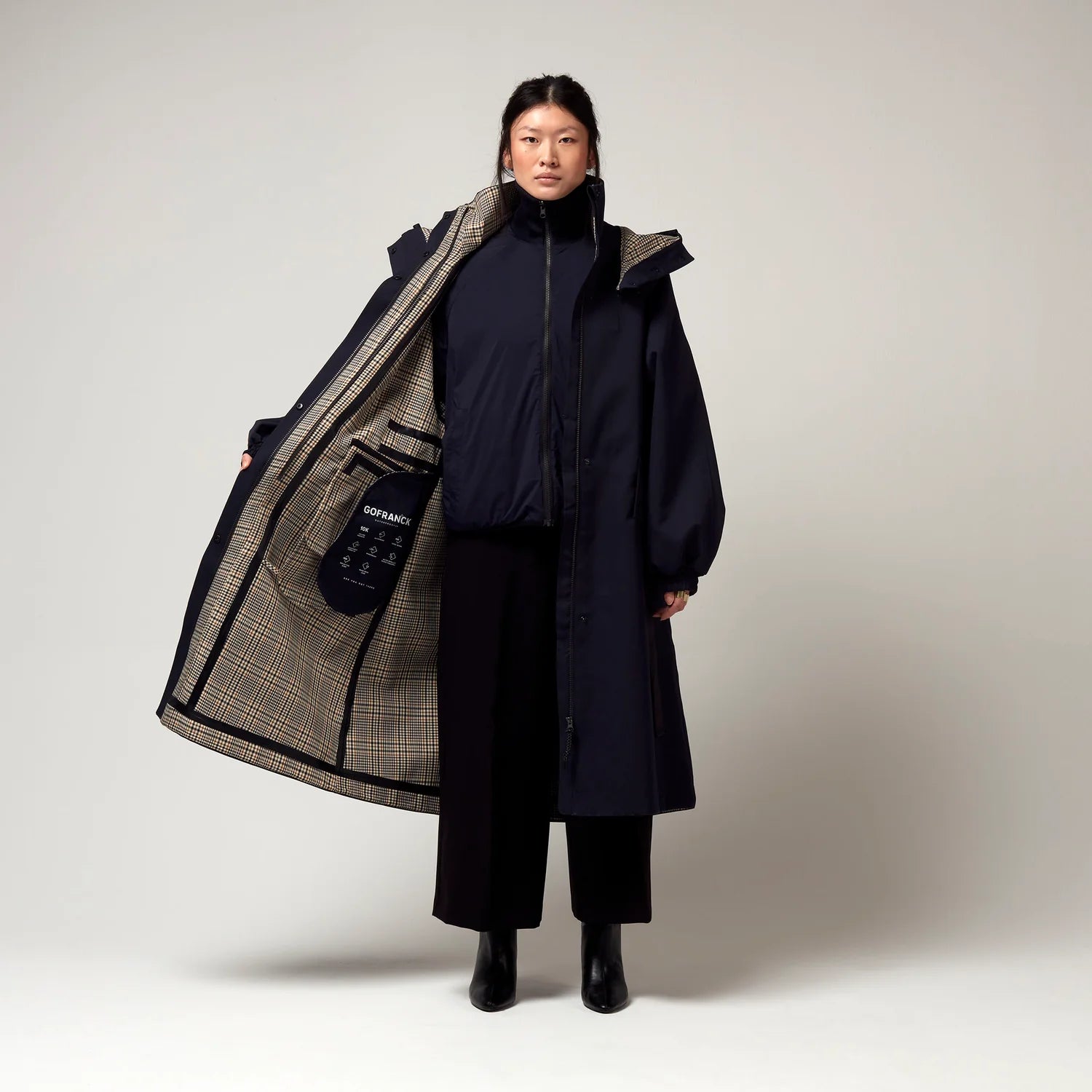 Dunkel Blauer Parker, mit Verstellbarer sowie abnehmbarer Kapuze, Geöffnete Jacke, Innenjacke geschlossen. Karo Muster sowie Innentaschen erkennbar. Model Bild, Ganzkörper Aufnahme.