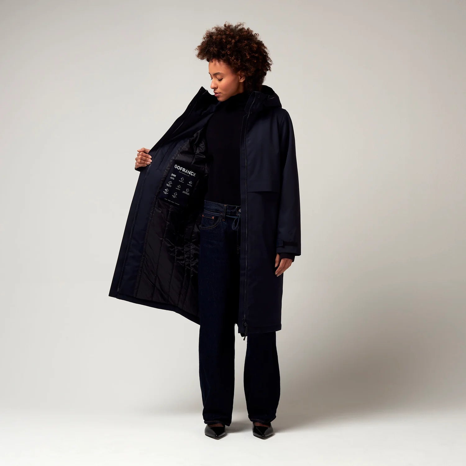 Dunkel Blauer Parker, mit verstellbarer Kapuze, Seitentaschen sowie Saum mit Daumen Loch. Glatte Oberfläche. Schwarze Hardware. Model Foto Ganzkörper Aufnahme, leicht geöffnete Jacke, Innenfutter erkennbar.