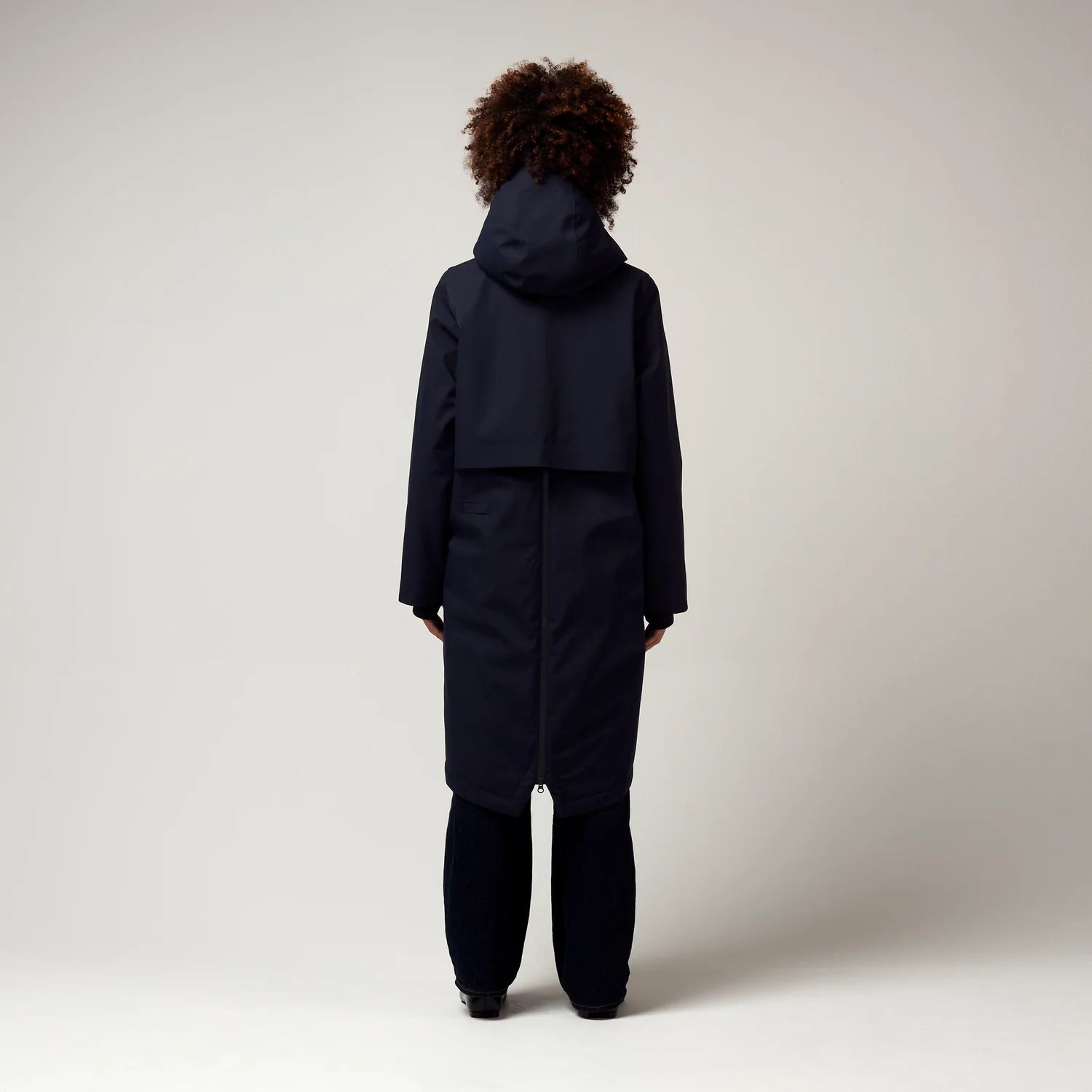 Dunkel Blauer Parker, mit verstellbarer Kapuze, Seitentaschen sowie Saum mit Daumen Loch. Glatte Oberfläche. Schwarze Hardware. Reißverschluss vom Saum der Jacke bis Hoch zum Oberen Rücken. Model Foto Ganzkörper Aufnahme, Rückseite. 