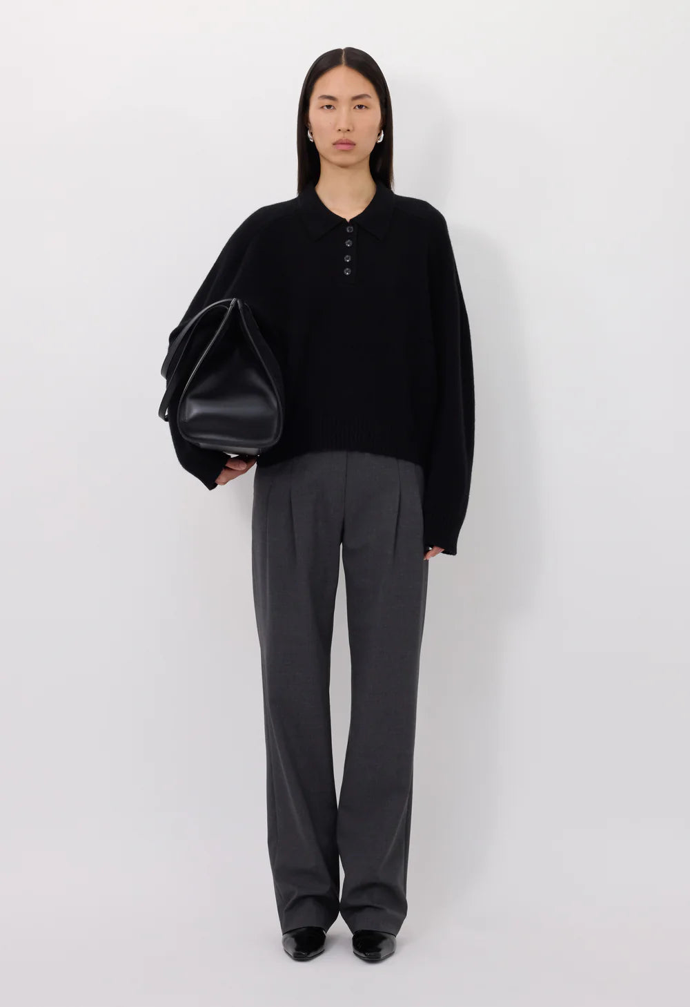 Model in der Halbtotalen. Sie hält in der rechten an eine Tasche und schaut geradeaus in die Kamera