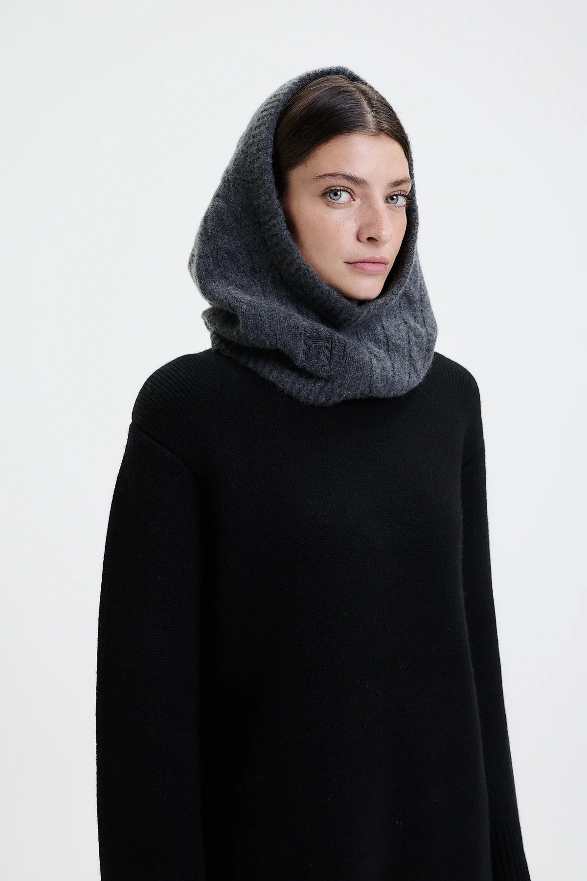 Prinz Berlin Kaschmir Balaklava in graphite mit Rippenstrick Optik. Das Model trägt die Balaklava zusammen mit einem schwarzen Pullover. Portrait des Models, seitlich.