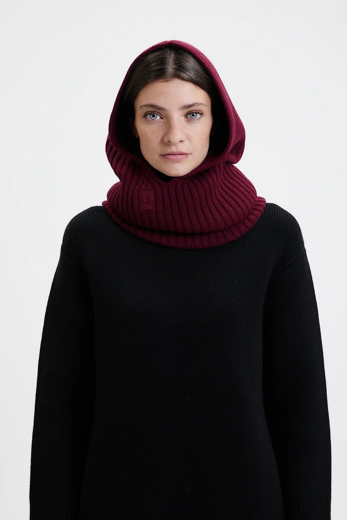 Prinz Berlin Kaschmir Balaklava in bordeaux mit Rippenstrick Optik. Das Model trägt die Balaklava zusammen mit einem schwarzen Pullover. Portrait des Models.