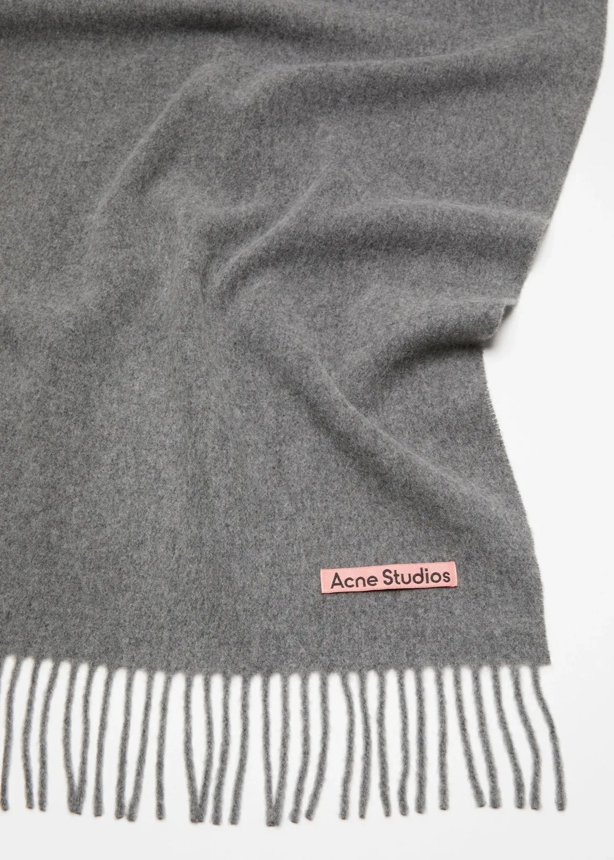 Fokus auf das rosafarbene Acne Studios Etikett und das ausgefranste Ende des Schals.