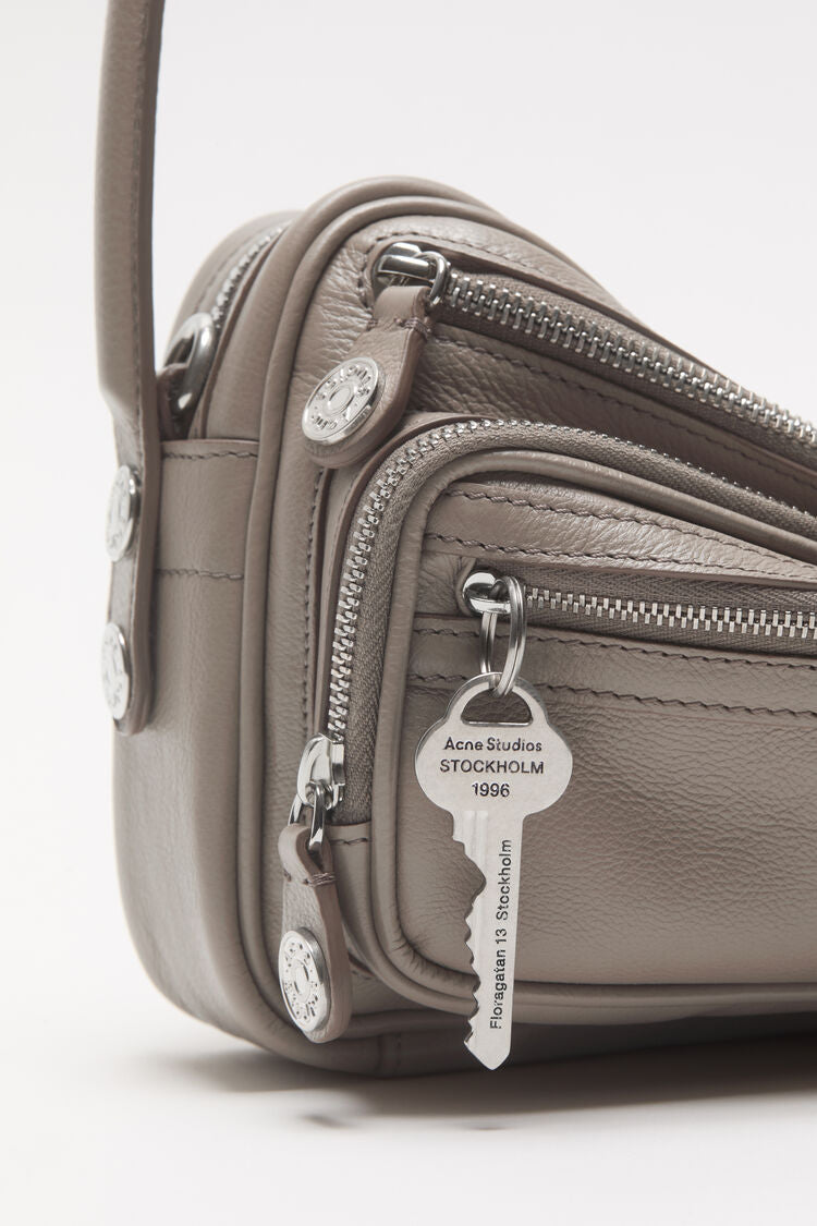 Beige Baguette Tasche mit Reisverschluss Details. Schlüsselanhänger an vorderem Reisverschluss Fach. Detail Shot Reisverschlüsse.