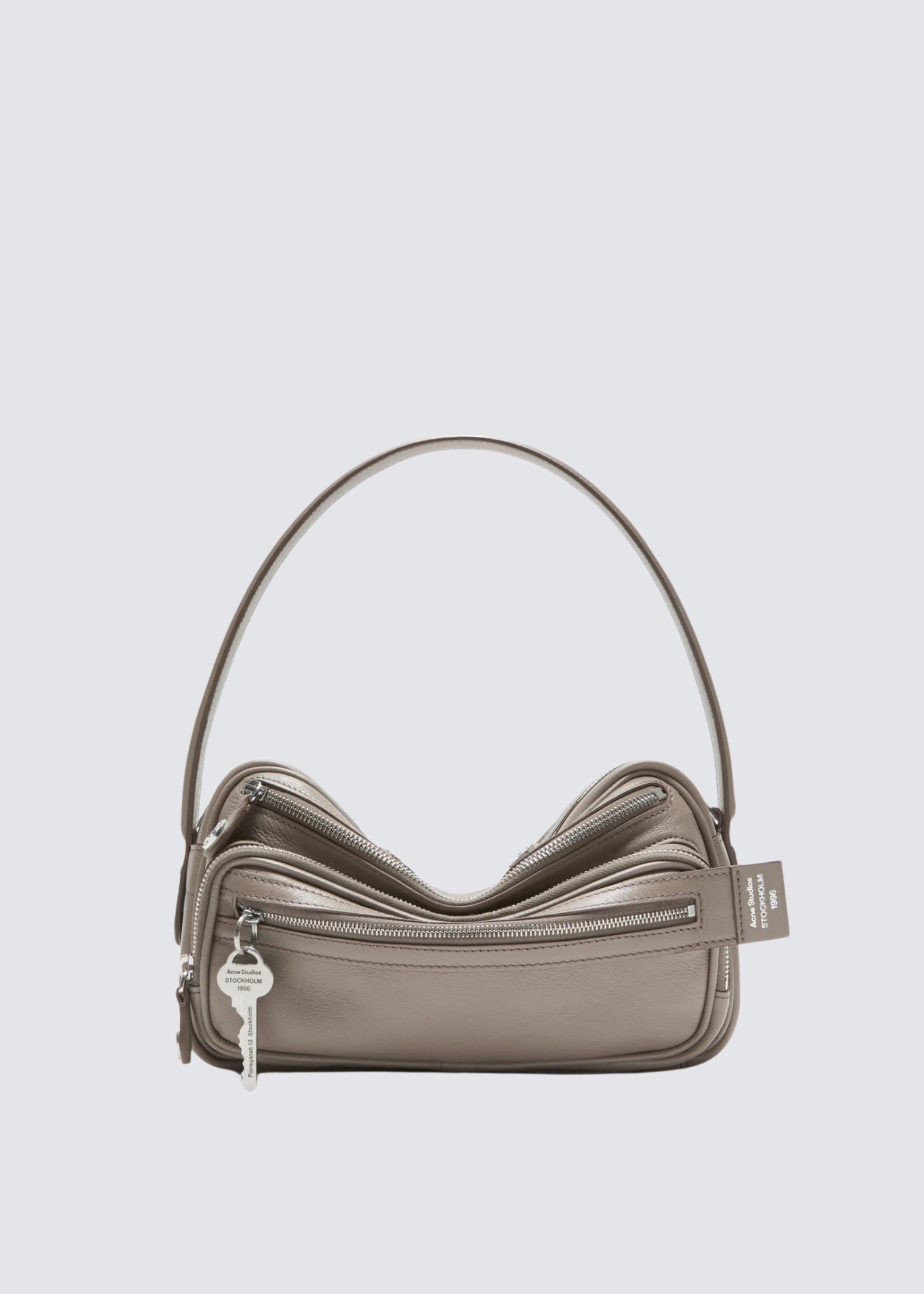 Beige Baguette Tasche mit Reisverschluss Details. Schlüsselanhänger an vorderem Reisverschluss Fach. Flatshot.