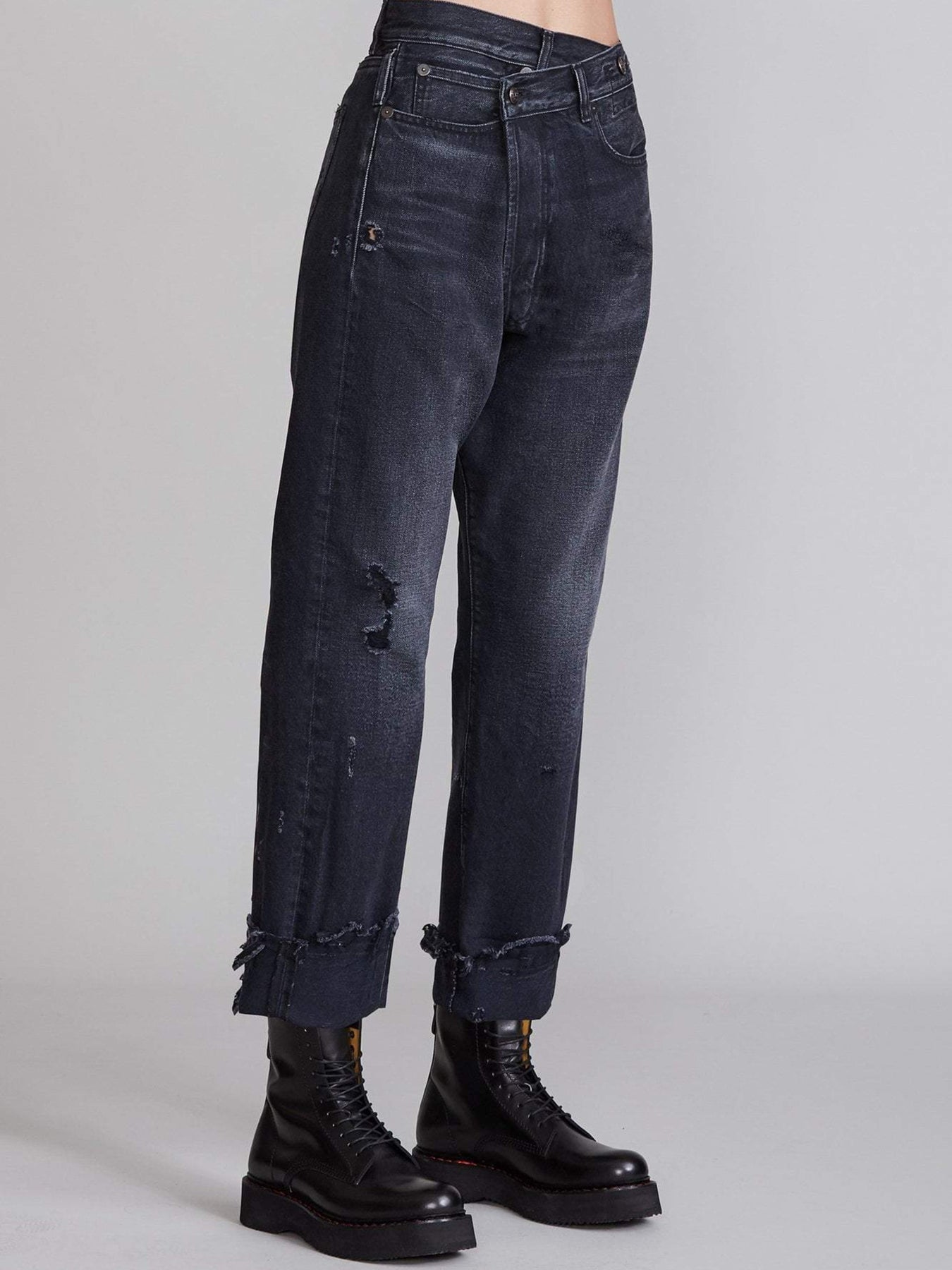 Das Model trägt die R13 Cross Over Jeans in Jake Black, Seitenansicht. 