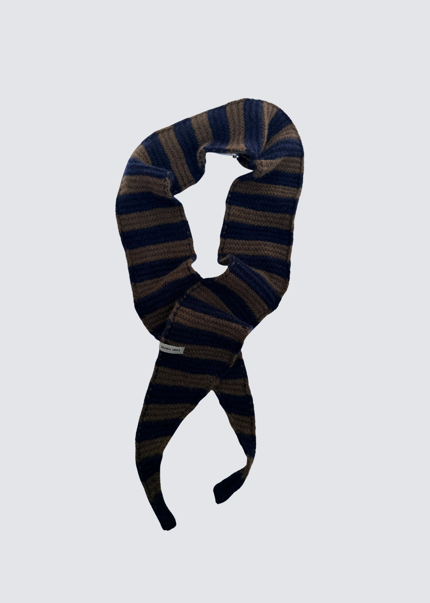 Gestrickter schmaler Schal in Braun und Maine Farben. Spitz zulaufend. Dezentes Studio 1893 Logo am Ende des Schals. Flatshot. 