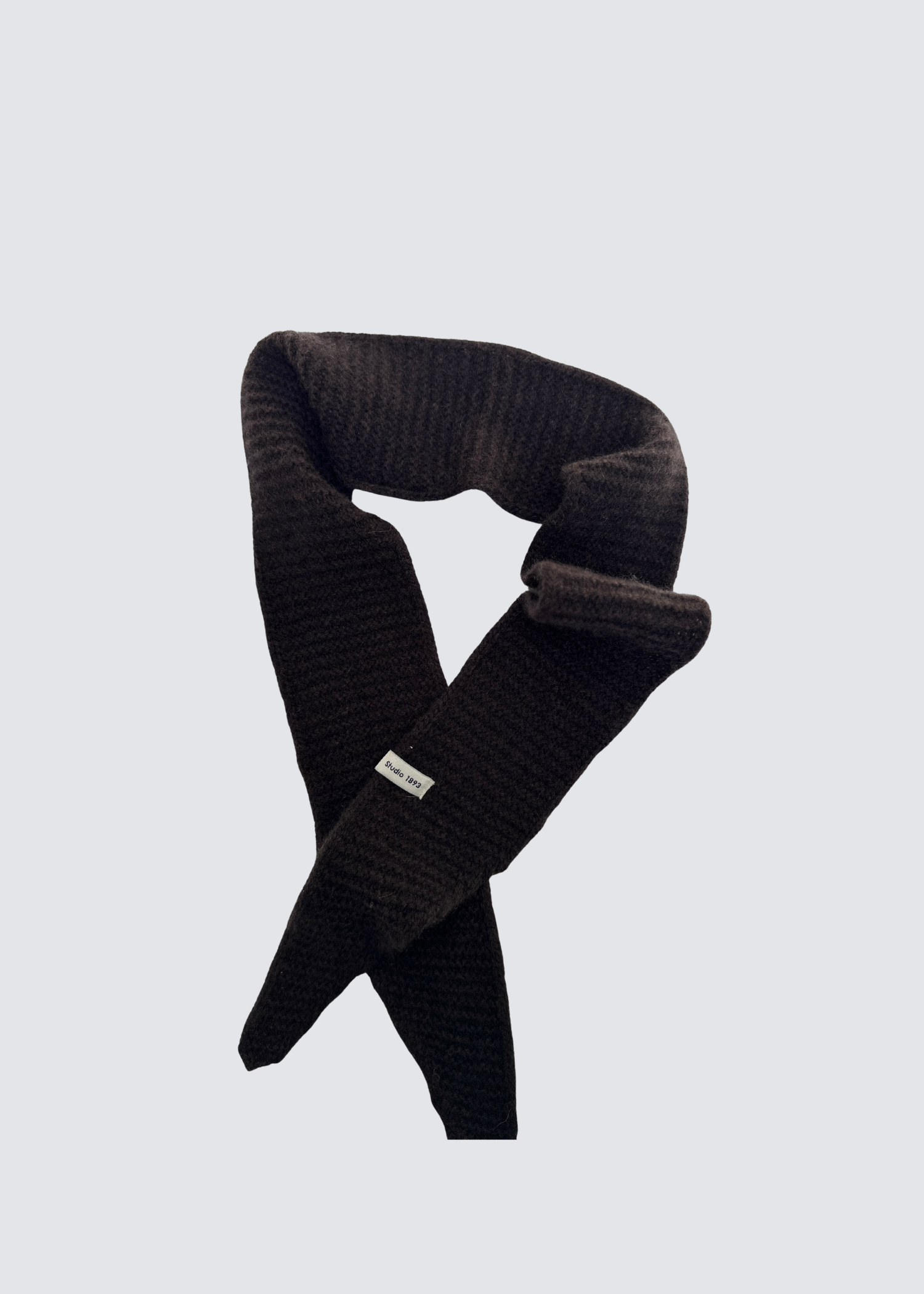 Gestrickter schmaler Schal in Braun . Spitz zulaufend. Dezentes Studio 1893 Logo am Ende des Schals. Flatshot.