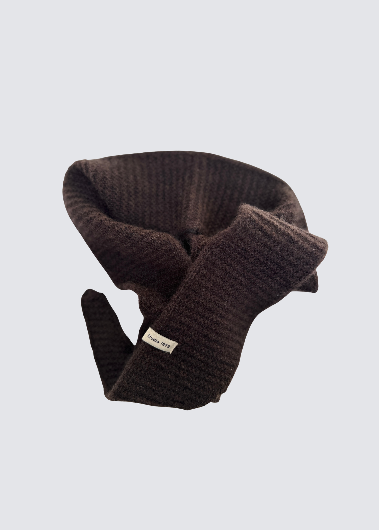 Gestrickter schmaler Schal in Braun . Spitz zulaufend. Dezentes Studio 1893 Logo am Ende des Schals. Flatshot.2