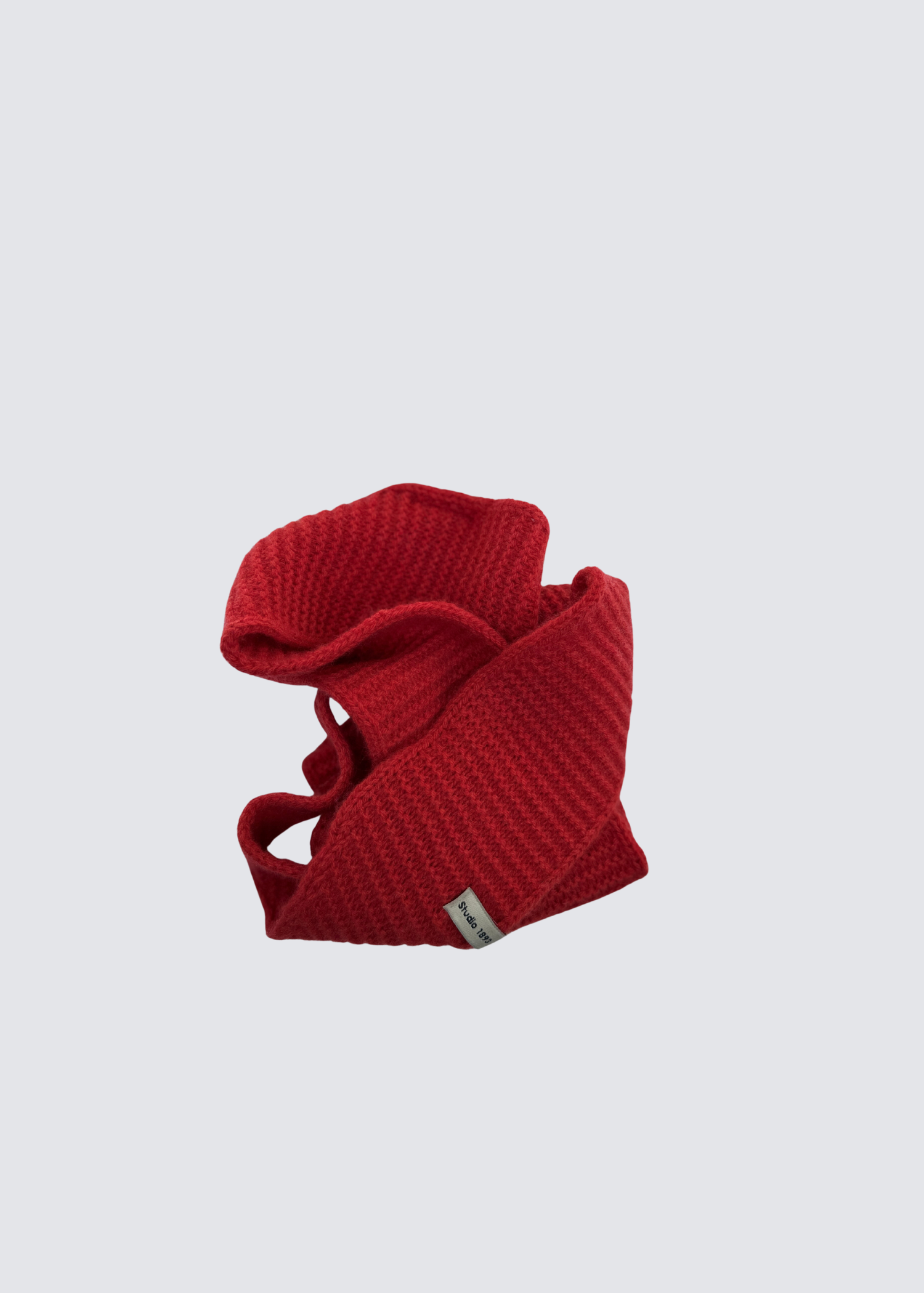 Gestrickter schmaler Schal in Rot . Spitz zulaufend. Dezentes Studio 1893 Logo am Ende des Schals. Flatshot, gewickelt.